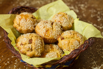 Salty muffins with sausage, cheese and sesame in basket on brown wood table.