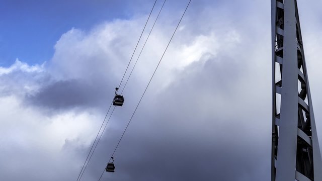 Timelapse narrow view of cable cars over the river Thames in the financial district of the Docklands in London with dark clouds