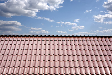 Gable roof of a house covered with metal tile closeup against blue sky with white clouds