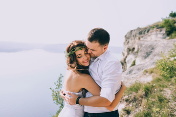 a happy married couple posing on the rock near the lake