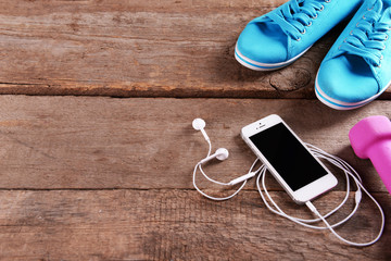 White cellphone with headphones and pink dumb bells and gumshoes on wooden background