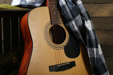 Acoustic guitar and blue checkered shirt against box with hay on wooden background, close up