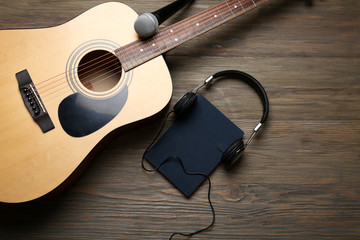 Acoustic guitar, headphones, notebook and microphone on wooden background