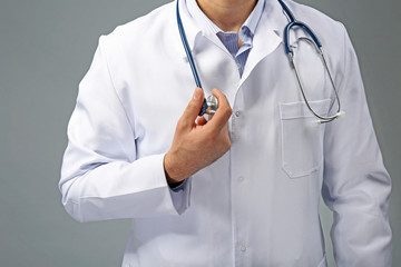 Doctor with crossed hands and stethoscope on grey background, close up