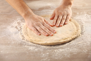 Hands preparing dough basis for pizza on the wooden table, close-up