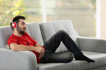 Handsome man listens music with headphones on grey sofa in the room