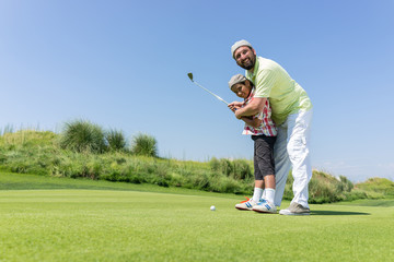 Father teaching son playing golf at club