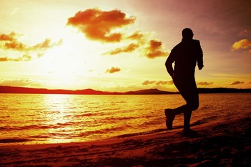 Fototapeta na wymiar Silhouette of sport active man running and exercising on beach at vivid colorful sunset.