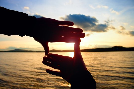 Holding hands in square frame with sunset immersing at the horizon. Autumn evening at the lake.