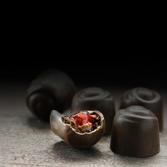 chocolate pralines with filling from red fruit jelly on a rustic