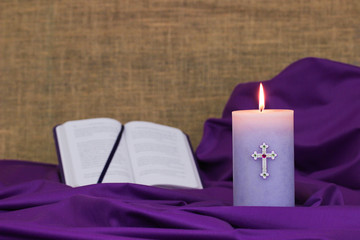 Purple Easter candle burning with fabric and bible blurred in background