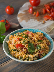 Schüssel mit Couscous und geschnittenen Tomaten im Hintergrund