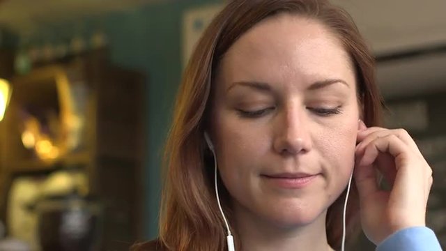 A happy young woman listening to music on headphones in a cafe