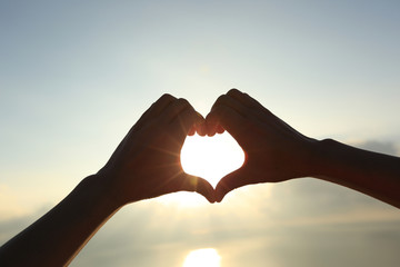 Plakat Heart shape making of hands against bright sea sunrise and sunny golden way at water