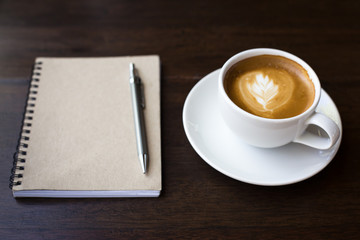 Coffee cup and notebook on grunge wooden background.