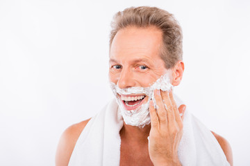 Handsome happy man with towel smearing shaving foam on his chin