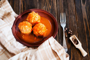 
lunch or dinner , meatballs with rice , carrots, onions , spices and tomato sauce on a wooden background