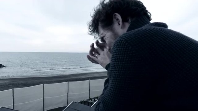 Closeup of sad lonely man crying desperate in front of the ocean