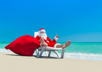 Obraz premium Santa Claus with Christmas sack on deckchair at ocean beach