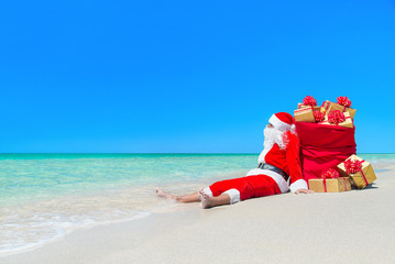 Christmas Santa Claus with sack of gift boxes at beach