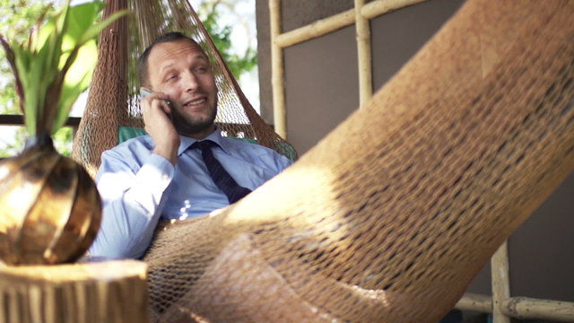Young businessman talking on cellphone on hammock, super slow motion 240fps
