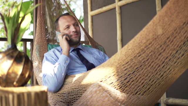 Young businessman talking on cellphone on hammock

