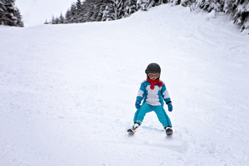 Fototapeta na wymiar Adorable little boy with blue jacket and a helmet, skiing wintertime