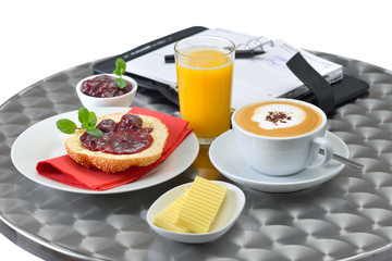 Kleines Bistrofrühstück mit Cappuccino und Orangensaft, ein geöffnerter Terminplaner im Hintergrund