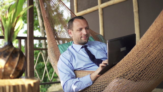 Young businessman working on laptop on hammock, super slow motion 240fps
