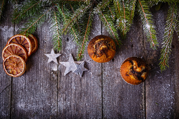 Xmas or new year composition with holiday decoration - Homemade christmas cupcakes, sliced dried oranges on wooden background with spruce twigs. Christmas card. Space for text. Rustic style