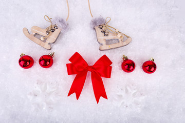 Xmas or new year composition with holiday decorations - little cristmas baubles on snow, red satin bow and toy skates on snow background. Christmas card