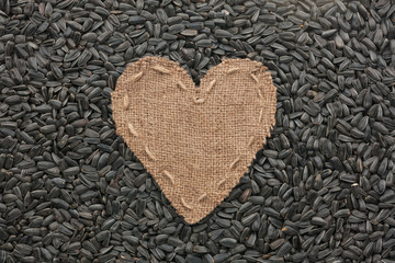 Frame in the shape of heart made of burlap with sunflower seeds