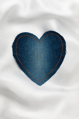 Heart made of denim fabric with yellow stitching on white silk