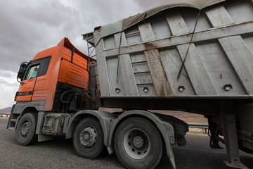 orange truck moves dirty dark industrial container in a dark overcast setting