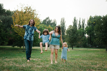Fototapeta premium Happy young hipster family having fun while running, bowl, rising up, piggyback ride their children in park on summer sunset 