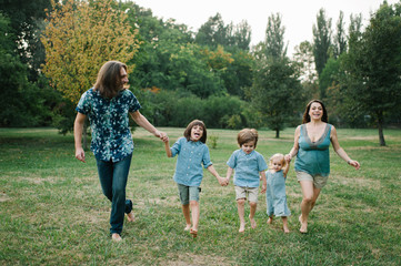 Obraz premium Happy young hipster family having fun while running, bowl, rising up, piggyback ride their children in park on summer sunset 