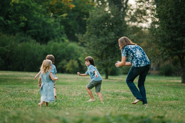 Happy young hipster family having fun while running, bowl,  rising up, piggyback ride their children in park on summer sunset
