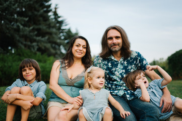 Happy young hipster family having fun, bowl,  rising up, piggyback ride their children in park on summer sunset
