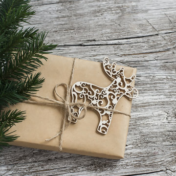 Homemade Christmas gift in kraft paper, wooden Christmas deer ornament, Christmas tree branches on rustic light wooden surface. Free space for text. Christmas wooden texture