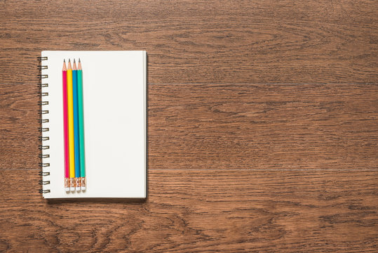 multicolor pencil with blank note book on wooden background