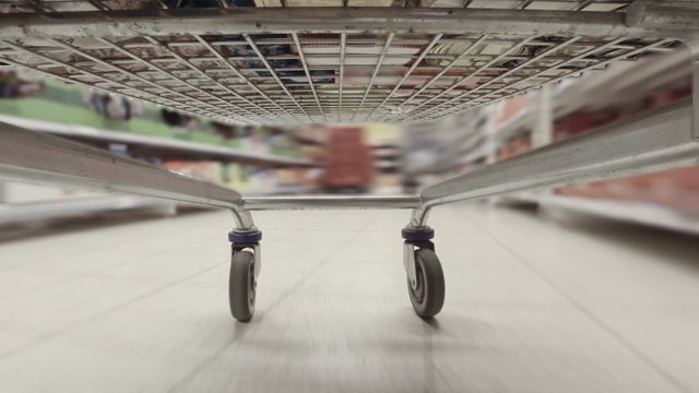 Busy view from underside of shopping trolley weaving between aisles in supermarket