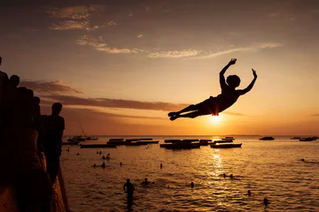 Foto op Canvas Silhouette of Happy Young boy jumping in water at sunset in Zanz © danmir12