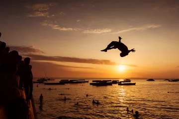 Fototapeten Silhouette eines glücklichen Jungen, der bei Sonnenuntergang in Zanz ins Wasser springt © danmir12