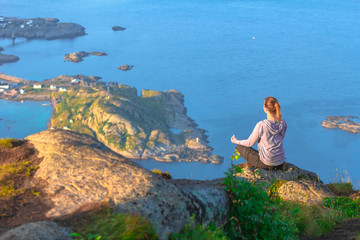 Young beautiful concentrated  woman doing yoga exerices on top of the mountain enjoying the breathtaking view over blue lagoon, green islands,small village and sunset