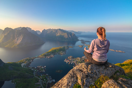 Young beautiful concentrated  woman doing yoga exerices on top of the mountain enjoying the breathtaking view over blue lagoon, green islands,small village and sunset