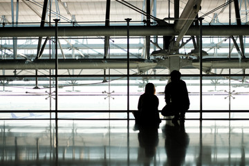 Silhouette of man and woman travelers waiting for plane at airport's hallway