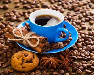 Close-up of coffee cup with roasted coffee beans on wooden backg