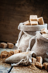 Cane brown sugar cubes and crystals in burlap sacks on old woode