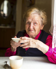 Happy old woman drinking tea in the kitchen.