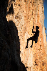 Silhouette of rock climber hanging on belay rope againstthe mountains
